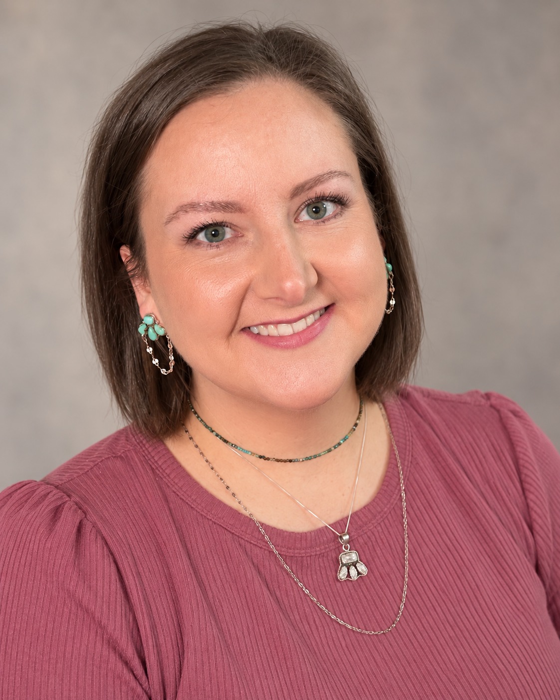Mallory Stone smiling, wearing a mauve blouse and turquoise earrings